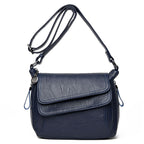 Navy blue soft leather crossbody bag with an adjustable strap, front flap pocket, and decorative metallic charm.