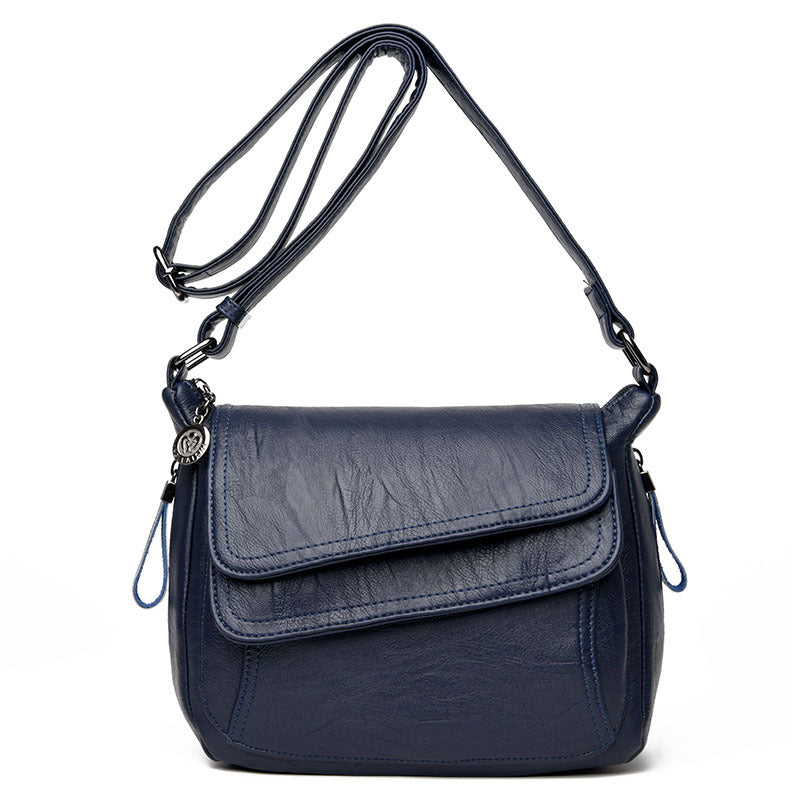 Navy blue soft leather crossbody bag with an adjustable strap, front flap pocket, and decorative metallic charm.