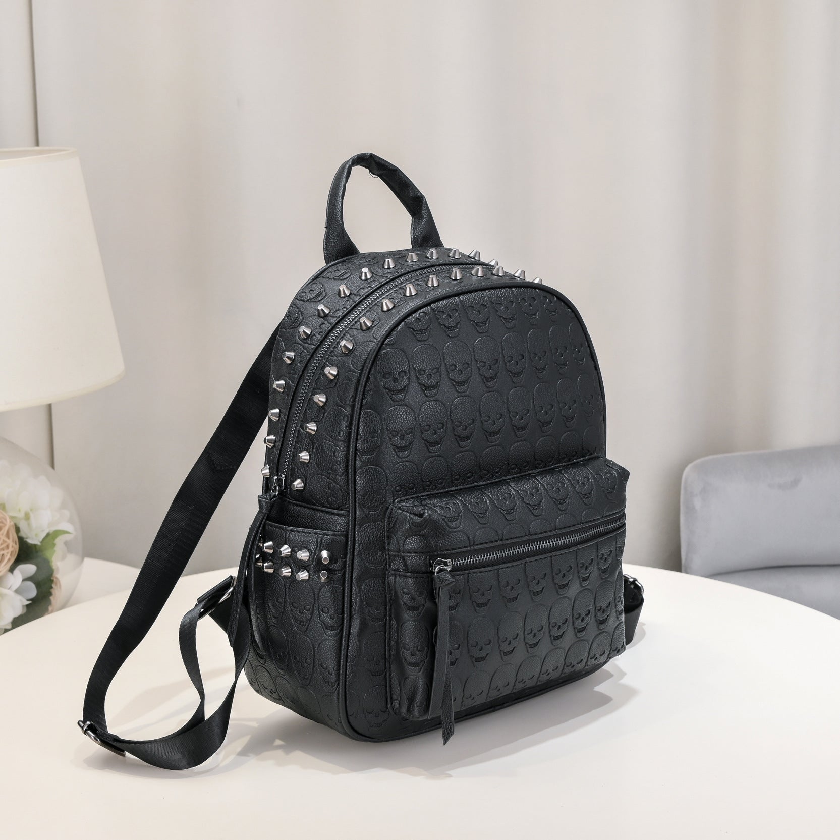 Black leather backpack with an embossed skull pattern, silver metal rivets, zip compartments, and adjustable straps.