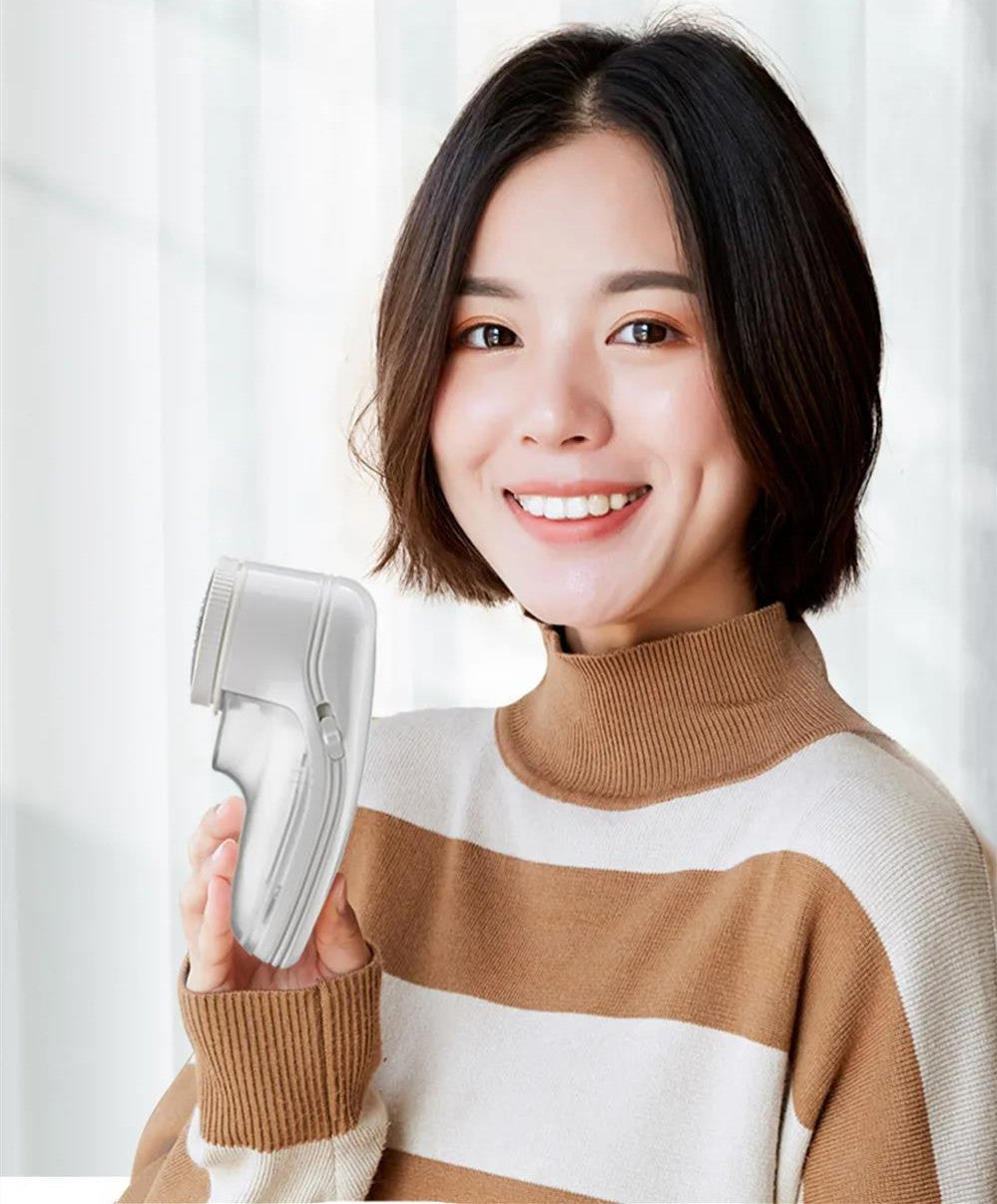 A smiling woman in a striped sweater holds a handheld, white plastic lint remover with a metal mesh head.