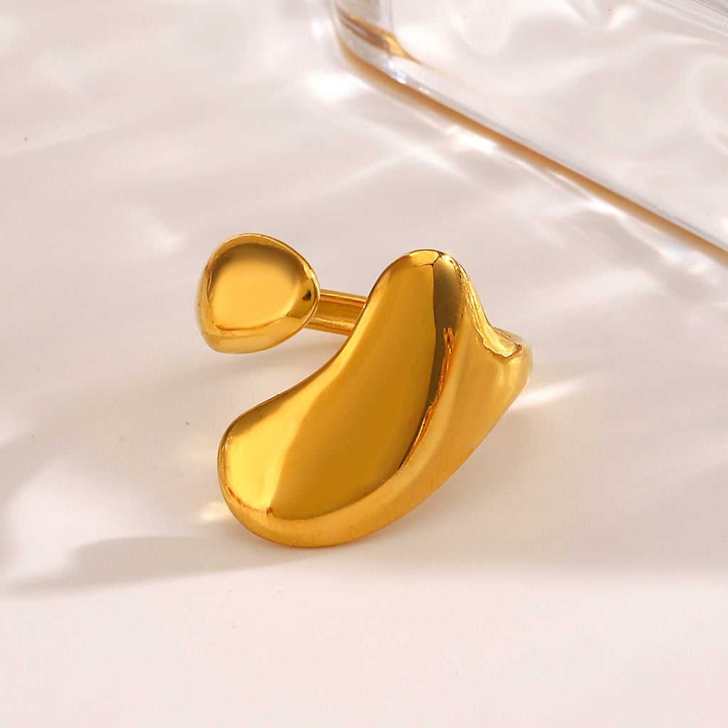 Gold-tone stainless steel ring with an open, asymmetric, organic liquid-shaped design on a reflective surface.