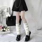 White knitted, ribbed-pile leg warmers worn with black loafers and a skirt, set against a cozy room backdrop.