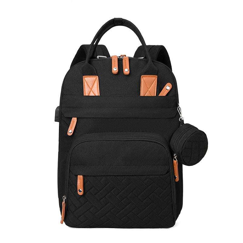 Black diaper backpack with tan leather accents, quilted front pocket, side USB port, and detachable circular pouch.