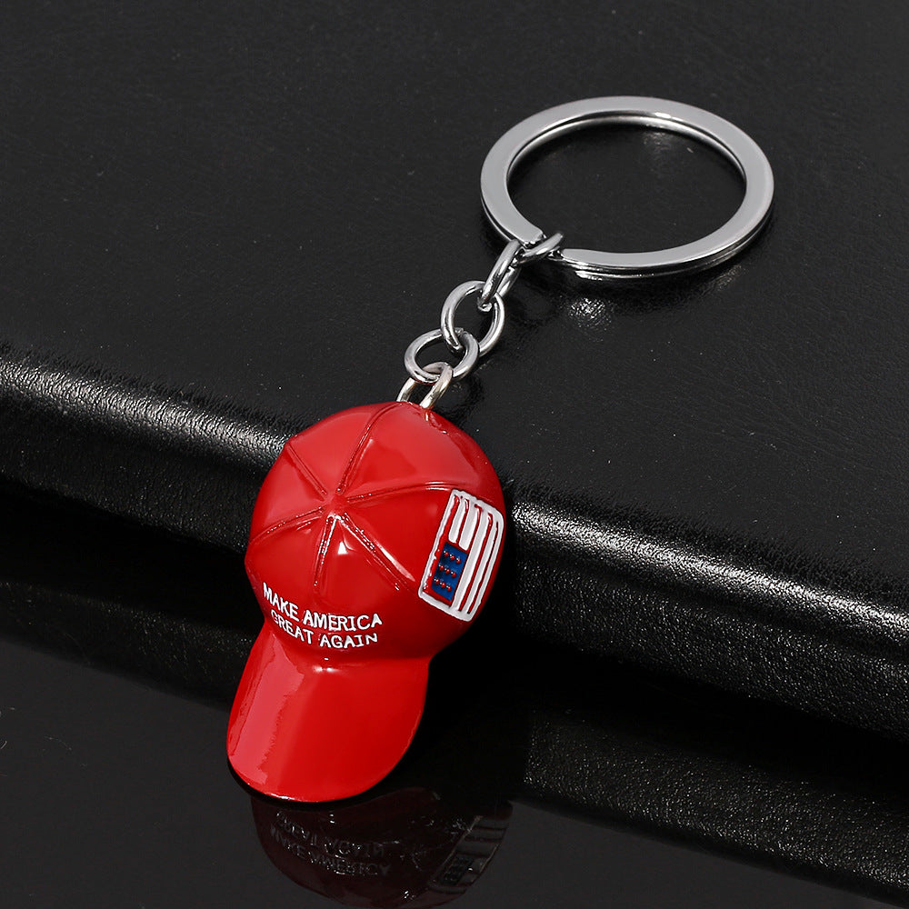 Red enamel "Make America Great Again" hat keychain with a silver metal ring, featuring a small American flag detail.