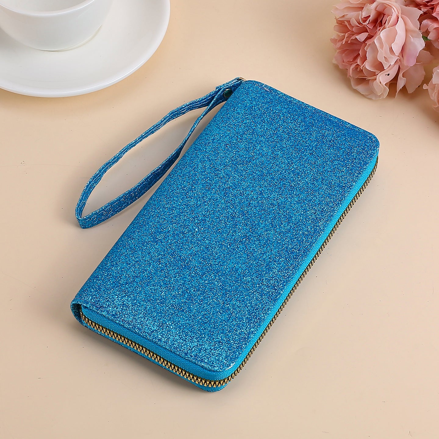 Blue glittery zip-around women's clutch wallet with a matching wrist strap, set on a light background.