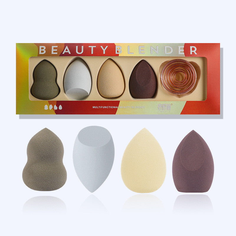 Set of four colorful makeup sponges in varied shapes and one spiral metal stand, presented in a retail gift box.