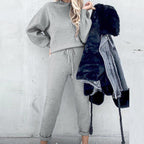 A woman wearing a cozy gray fleece long-sleeve sweater and matching drawstring joggers, holding a faux-fur denim jacket.