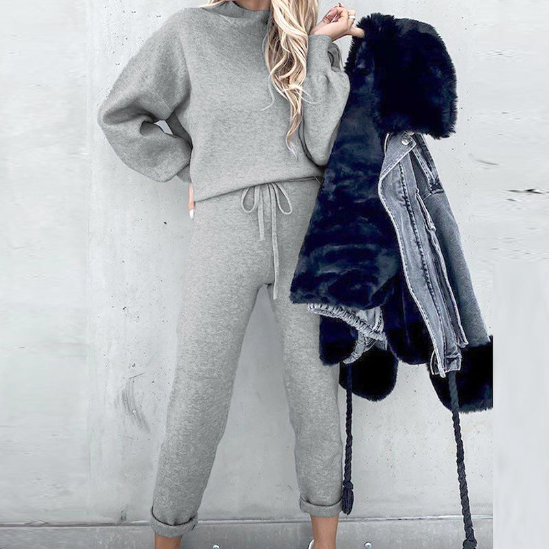 A woman wearing a cozy gray fleece long-sleeve sweater and matching drawstring joggers, holding a faux-fur denim jacket.