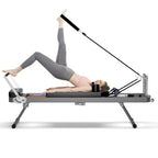 A person uses a foldable black Pilates reformer with metal frames and pulleys to perform a leg exercise.