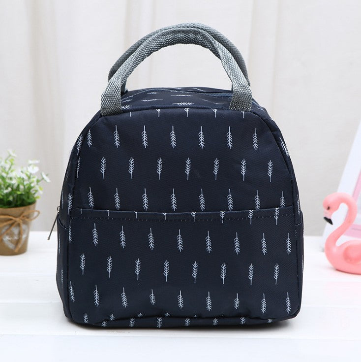Navy blue insulated lunch bag with white branch print, grey webbed handles, and front pocket, on a white table.