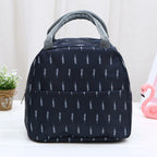 Navy blue insulated lunch bag with white branch print, grey webbed handles, and front pocket, on a white table.