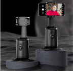 Two black 360-degree auto face-tracking smartphone gimbal mounts on grey pedestals against a dark, rippled background.