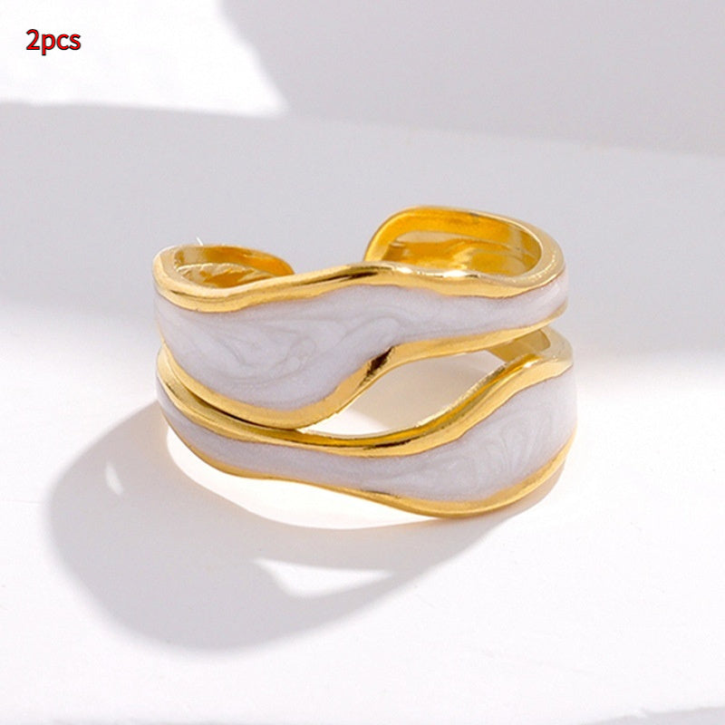 Two gold-tone titanium steel open rings featuring wavy white enamel accents, showcased against a light backdrop.