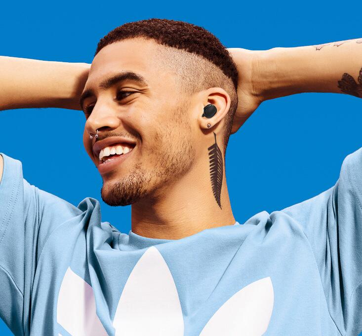 A smiling man wearing sleek, matte black A6S in-ear wireless headphones against a vibrant blue background.
