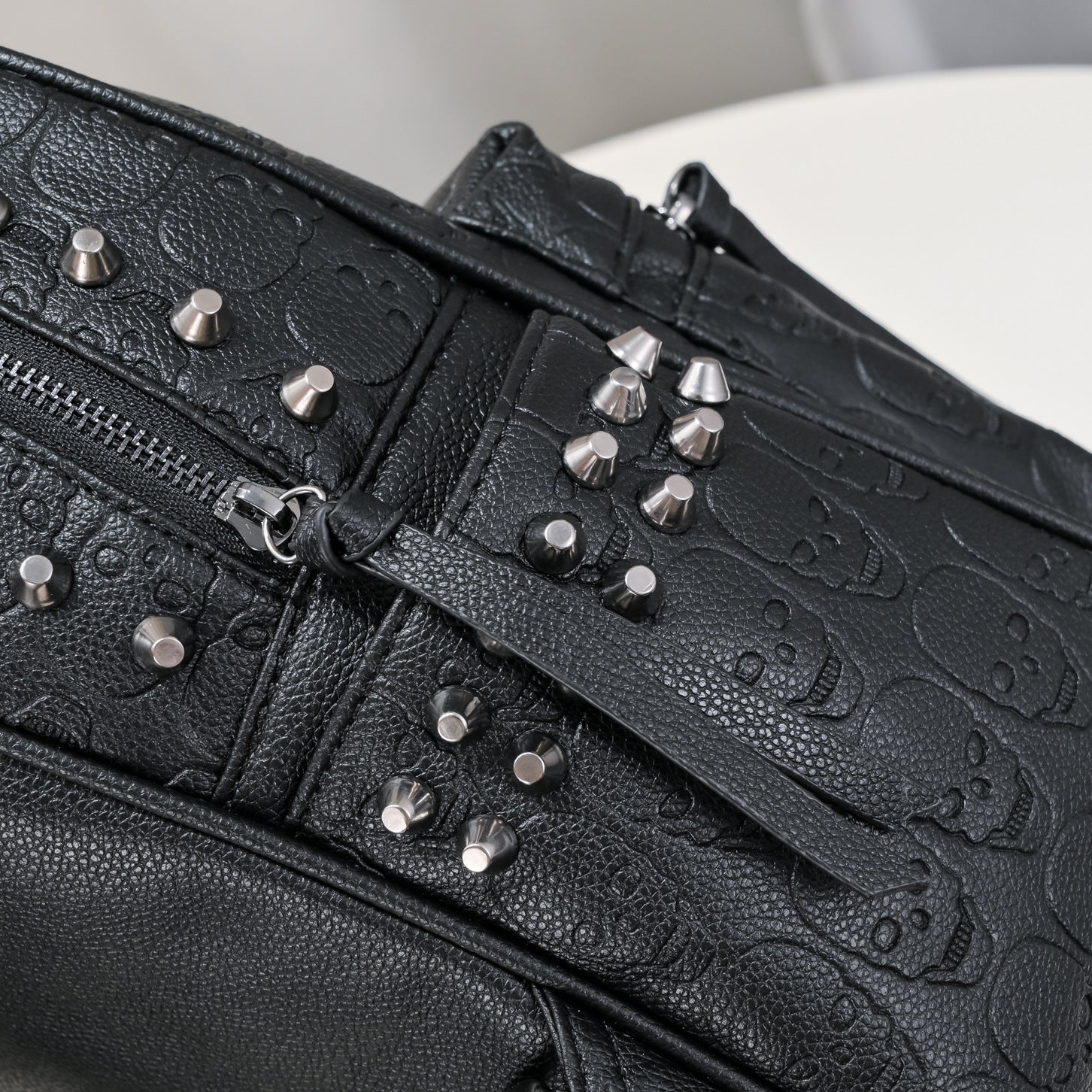 Black soft leather backpack with embossed skull patterns and silver metal rivet studs. Zipper closure visible.