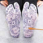 White reflexology socks with black printed acupuncture charts and a wooden massage tool pressing the sole.