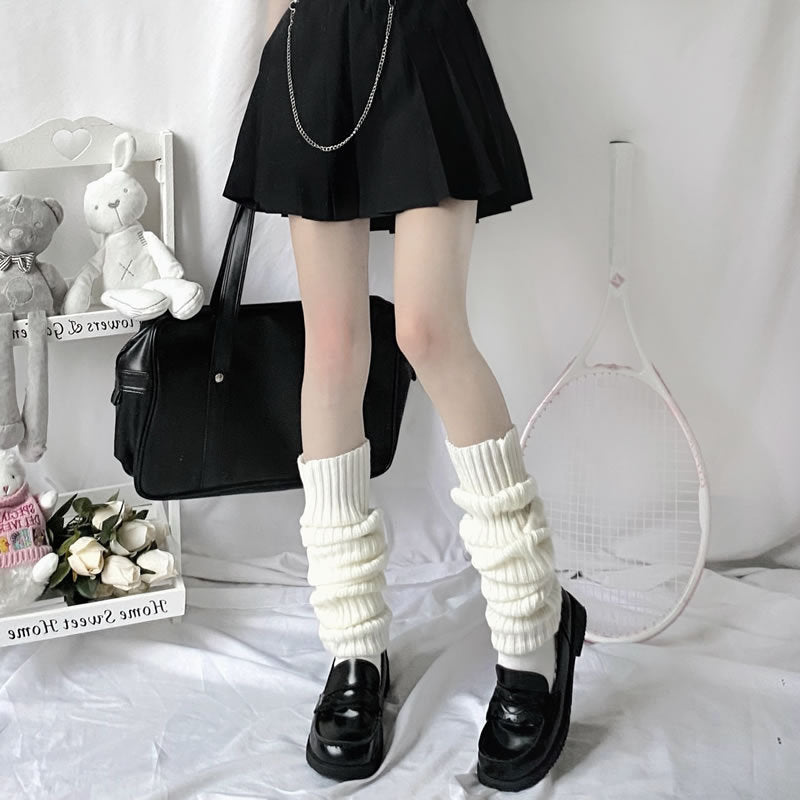 White ribbed knitted leg warmers worn over dark loafers, paired with a black pleated skirt and bag.