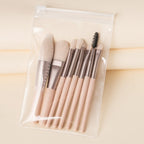 Set of 8 beige mini makeup brushes with metallic ferrules inside a clear, zippered travel pouch.