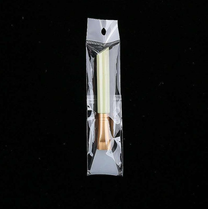 Silicone face mask brush with a pale green handle and gold ferrule, sealed in a clear plastic retail package.