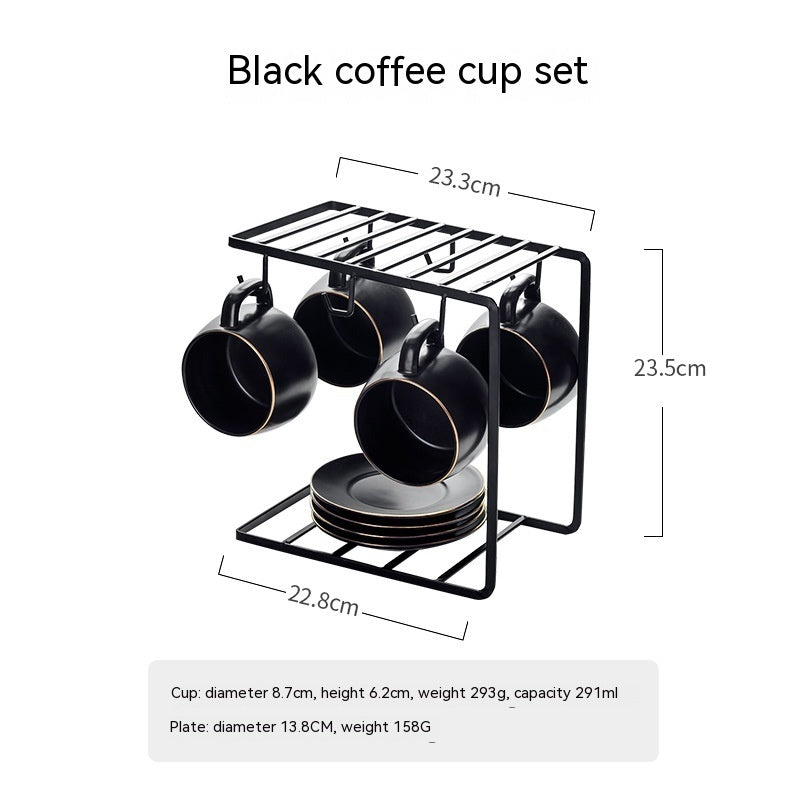 A matte black ceramic coffee cup set with gold rims, hanging on a matching black wire rack with a stack of saucers.