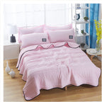 Soft pink cooling summer quilt with quilted texture and dark piped edges on a bed with matching pillows.