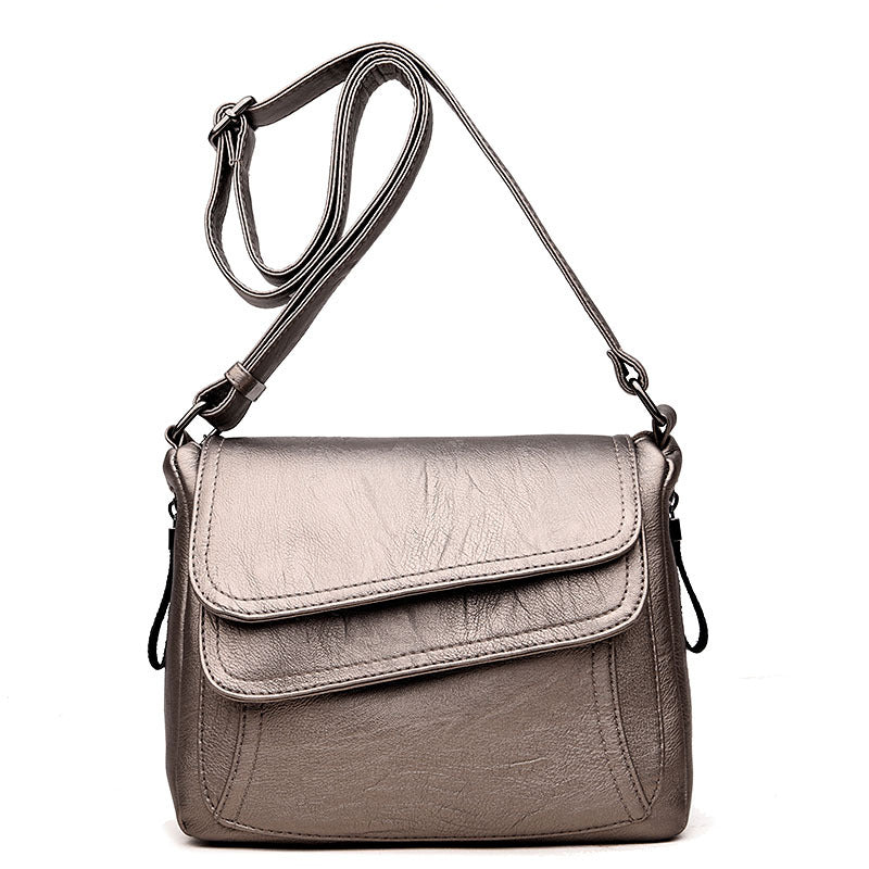 Metallic silver soft leather crossbody bag with an adjustable strap, fold-over flap, and structured silhouette.