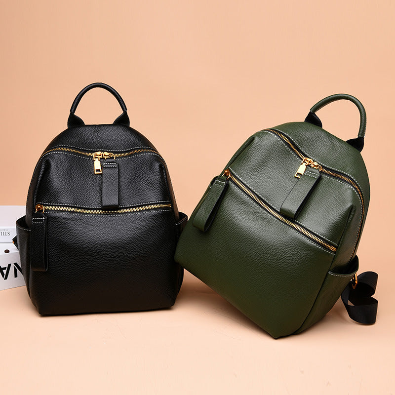 Black and green pebbled leather mini backpacks with gold zippers, top handles, and side pockets on a tan background.