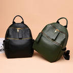 Black and green pebbled leather mini backpacks with gold zippers, top handles, and side pockets on a tan background.