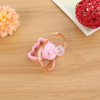 Pink silicone baby pacifier with a clear round head and handle on a wooden surface, next to a pink decorative orb.
