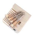Set of 12 champagne-colored synthetic makeup brushes with white bristles in a cream-colored leather storage roll.