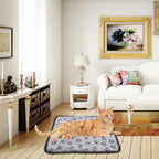 Orange cat lying on a grey, waterproof electric heating pad with black paw prints in a furnished living room.