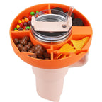 Orange 4-compartment silicone snack tray fitted onto a pale pink tumbler filled with assorted snacks and a straw.