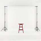 Adjustable black metal backdrop stand holding a seamless white fabric screen with a wooden stool in the center.