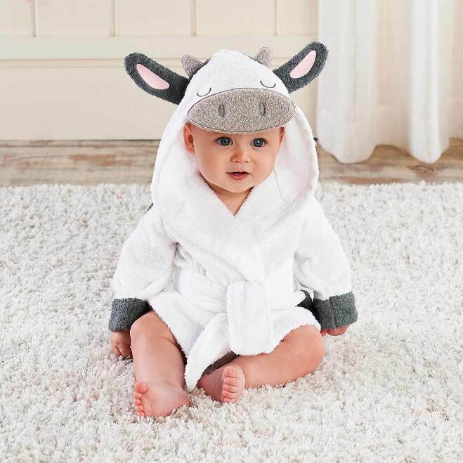 Baby wearing a white hooded cotton cow bathrobe with gray ears, horns, and trim, sitting on a soft white rug.