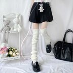 Person wearing white ribbed knit leg warmers, a black skirt, and black loafers. Aesthetic room with plush toys.