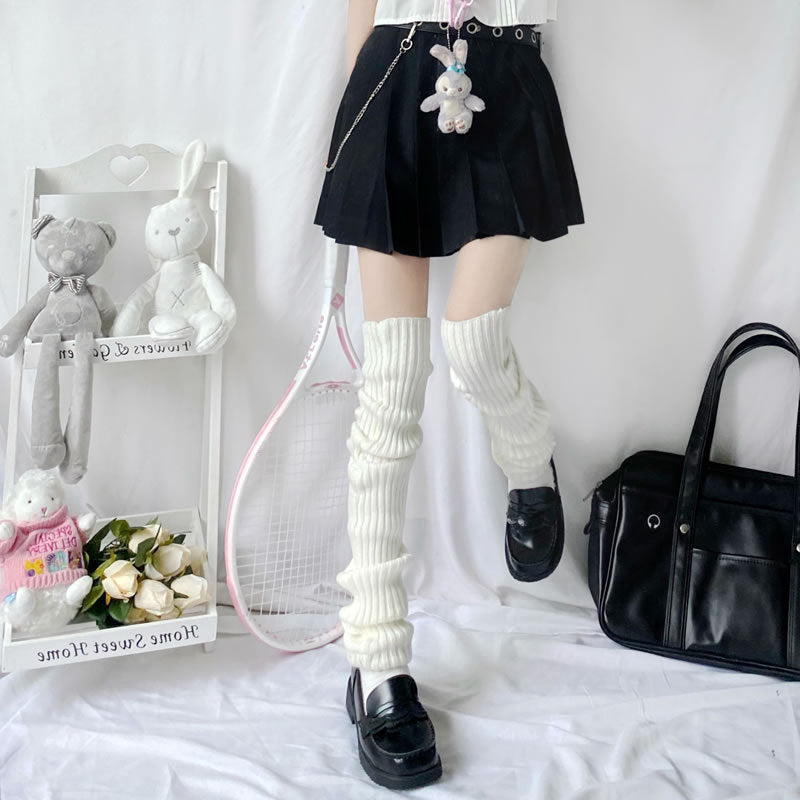 Person wearing white ribbed knit leg warmers, a black skirt, and black loafers. Aesthetic room with plush toys.