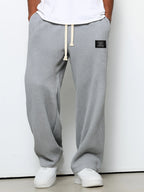 Loose grey waffle-knit men's trousers with a drawstring waist and a small rectangular brand patch.