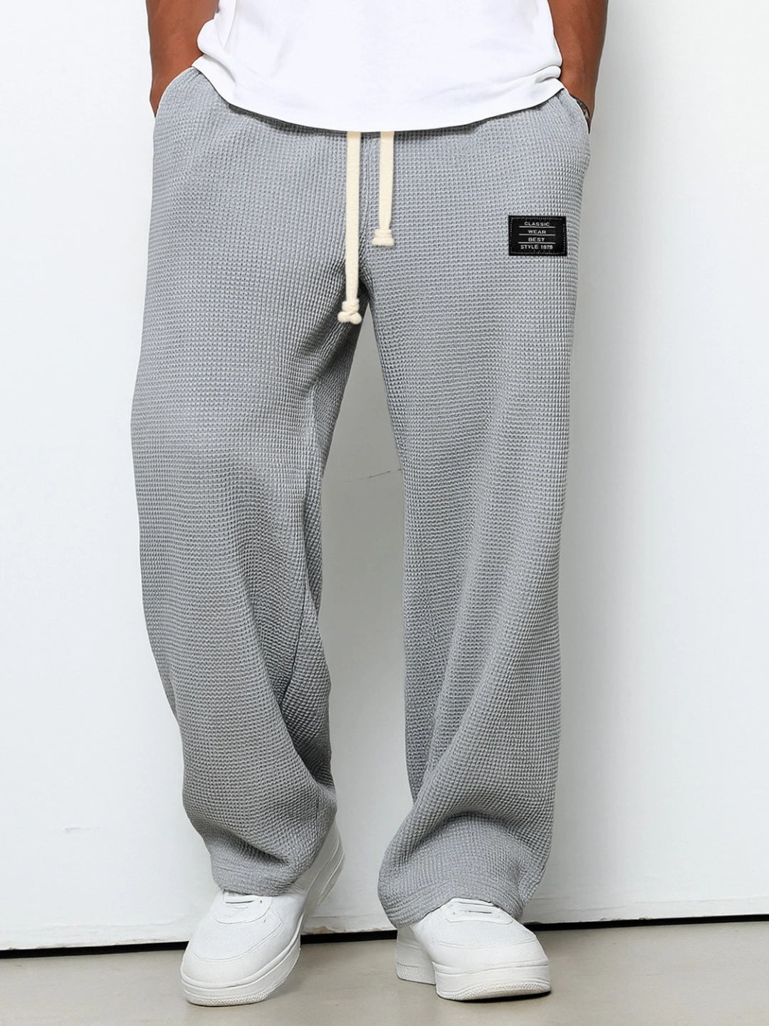 Loose grey waffle-knit men's trousers with a drawstring waist and a small rectangular brand patch.