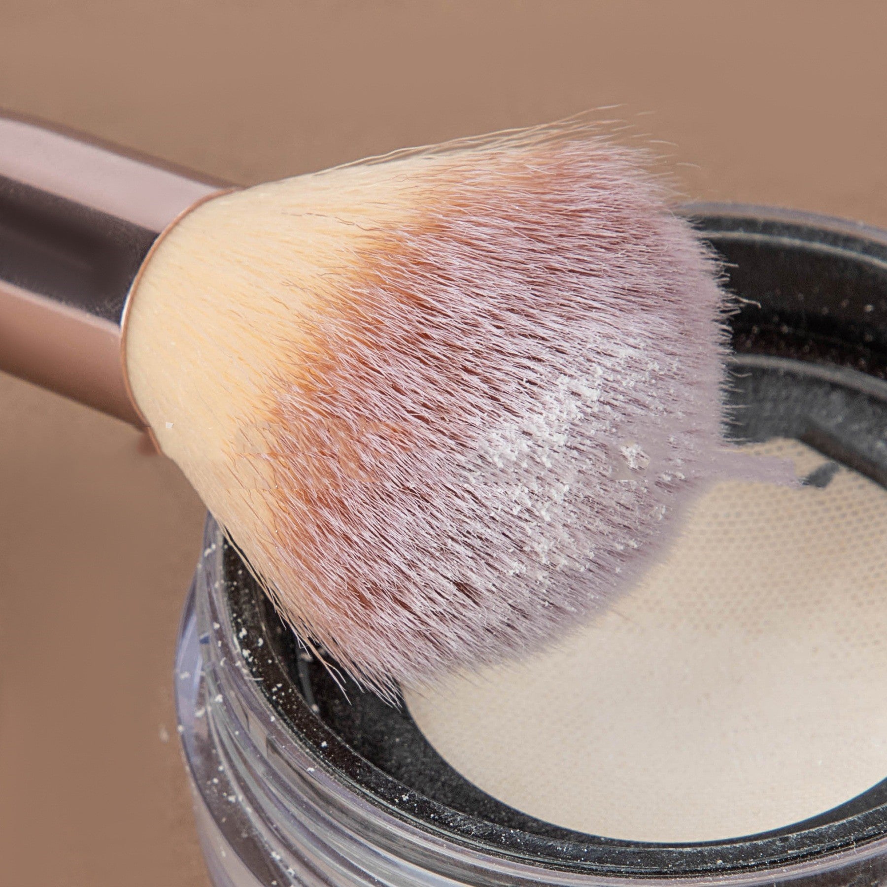 Makeup brush with soft bristles coated in loose powder hovering over a container of white foundation powder.