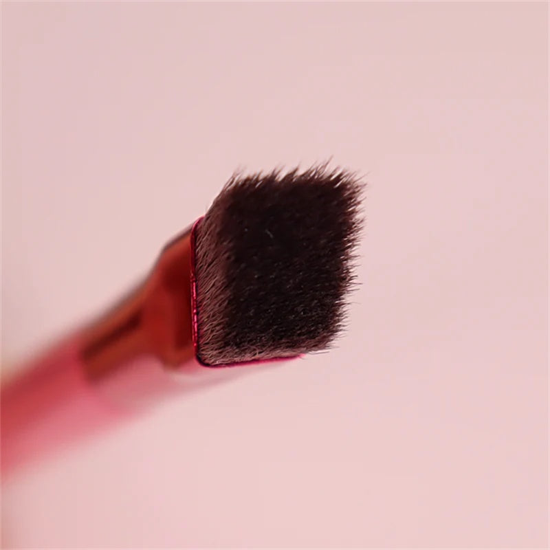 Close-up of a squared-off, angled eyebrow makeup brush with dark bristles and a metallic pink handle on a pink background.
