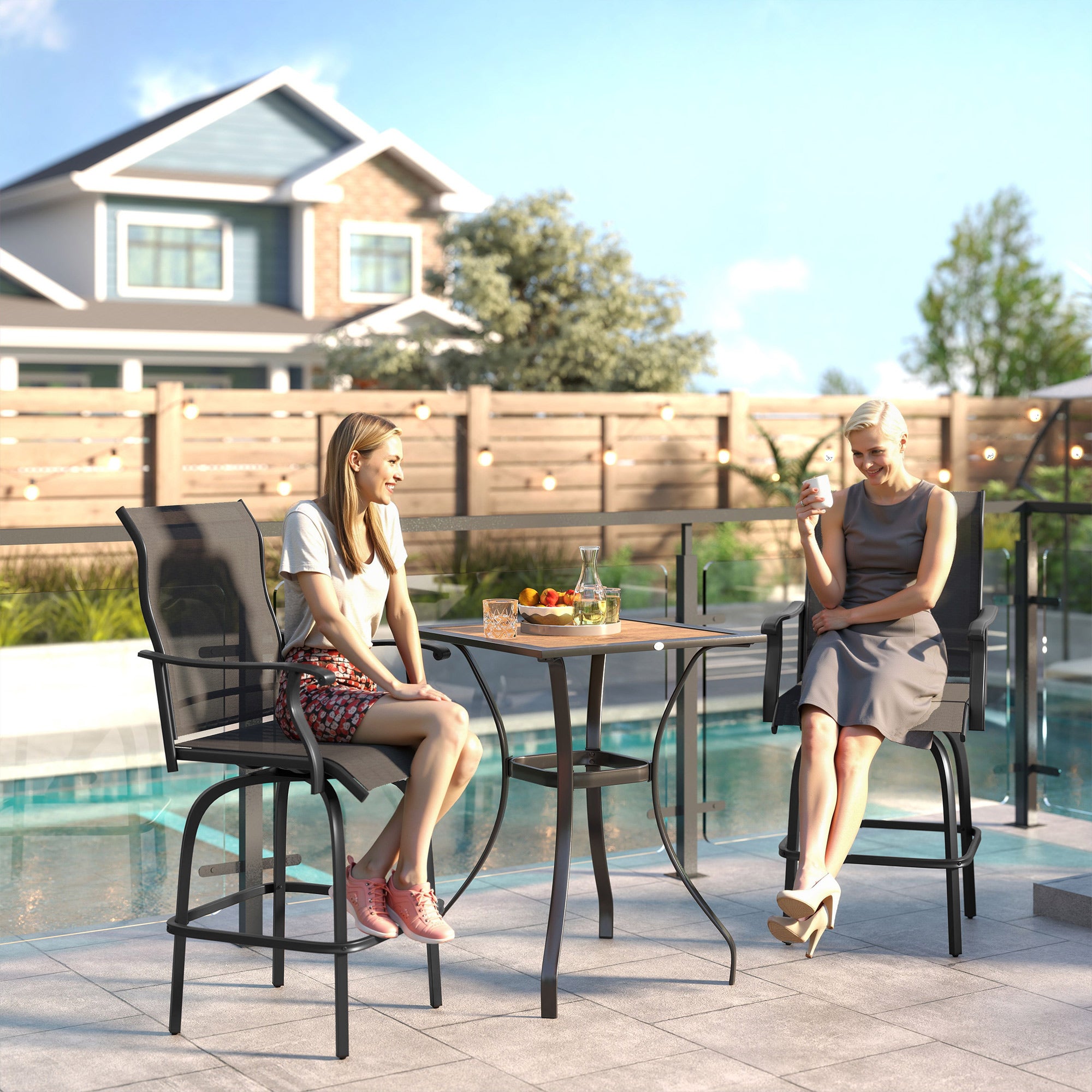 Two black metal swivel bar stools with sling seats and armrests on a patio by a pool, occupied by two women.
