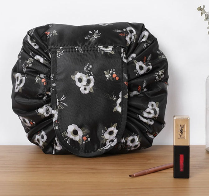 Black floral drawstring cosmetic bag on a wooden table, next to a lipstick and makeup brush.