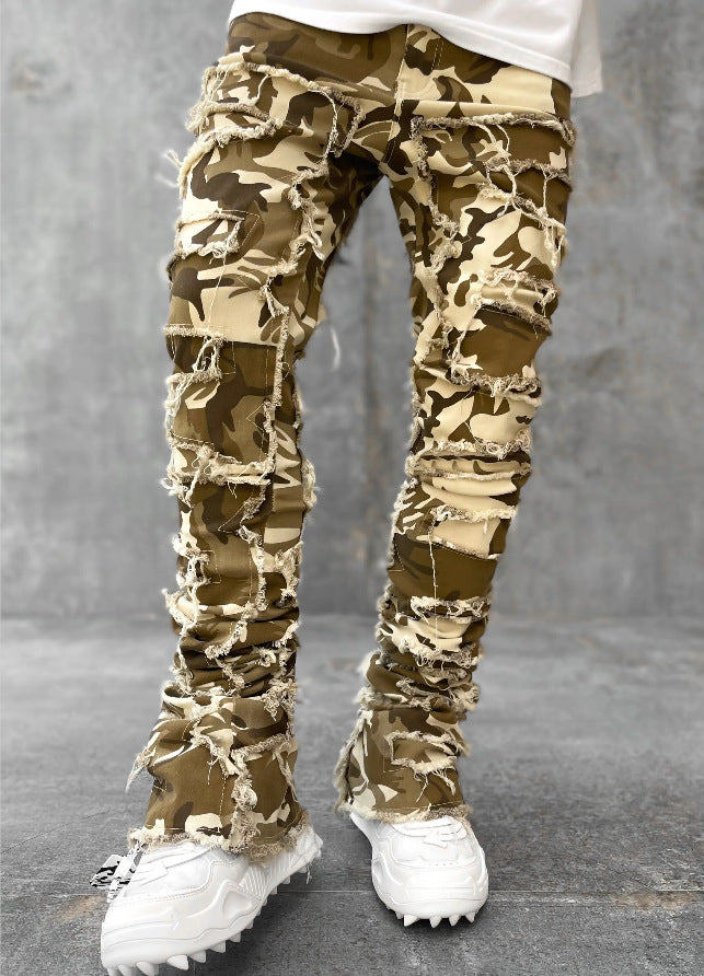 Men's tight-fit camo jeans with distressed fringe detailing, patchwork panels, and a stacked hem design.