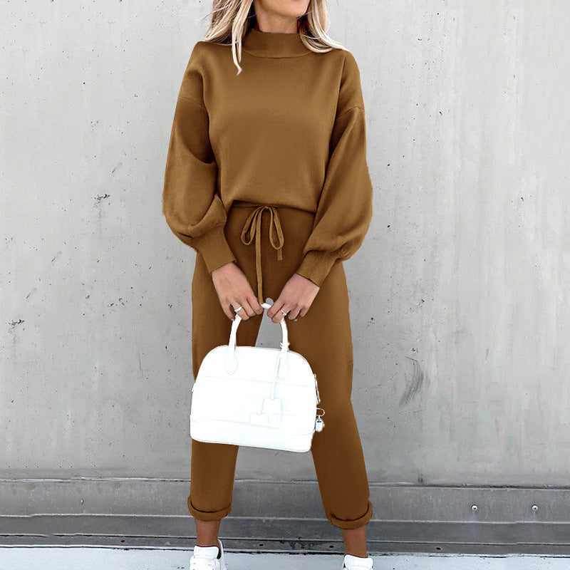 Woman wearing a brown fleece sweater suit with long sleeves, high neck, and drawstring joggers, holding a white bag.