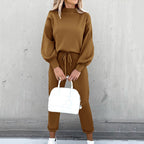 Woman wearing a brown fleece sweater suit with long sleeves, high neck, and drawstring joggers, holding a white bag.