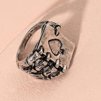 Silver-tone hip-hop ring featuring a skeleton hand clutching an ace of spades playing card on a soft pink background.