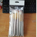 Set of 12 creamy white synthetic makeup brushes with champagne gold handles, packaged in a clear plastic bag.