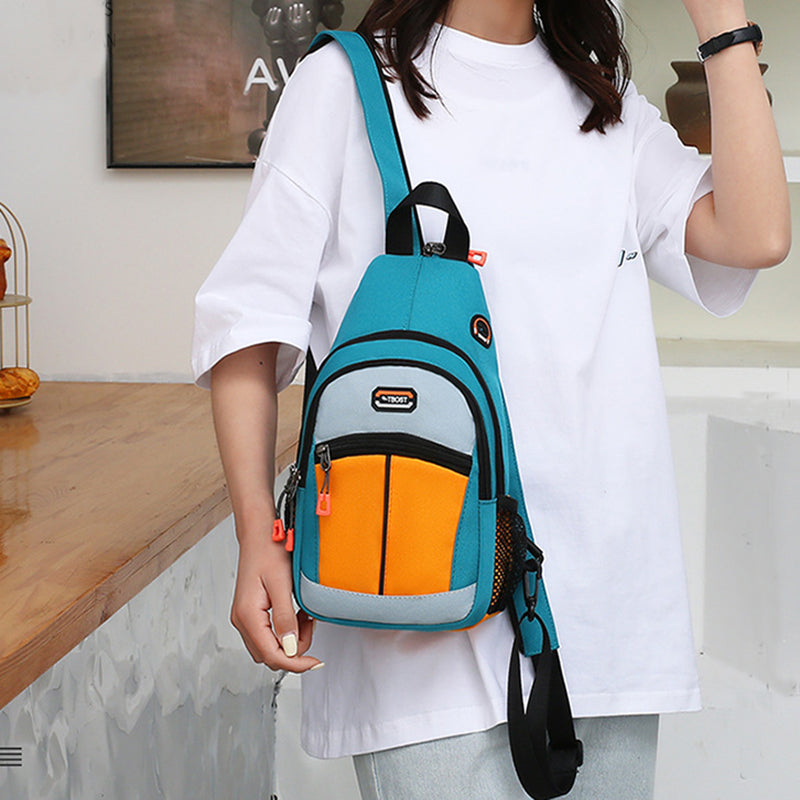 Woman wearing a teal, orange, and grey crossbody sling backpack with a USB port and mesh side pocket.