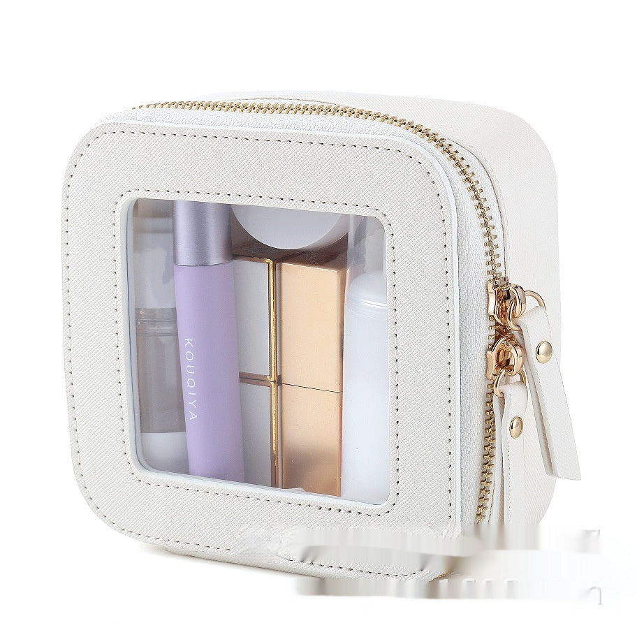 Small white square PU leather cosmetic bag with a transparent window, gold zipper, and visible beauty products inside.