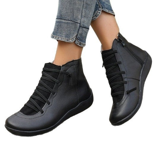 Black faux leather short boots with flat soles, side zippers, and decorative laces, worn with blue jeans.